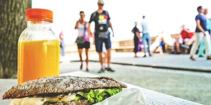 Picture shows a table with a bread roll and a couiple of joggers running past. It is a street scene