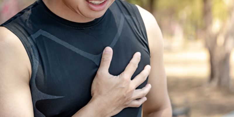 A person wearing exercise clothing outdoors and clutching their chest