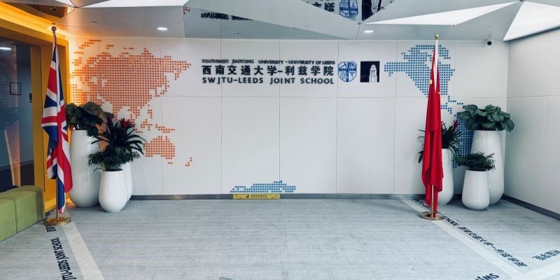 The foyer of the SWJU-Leeds Joint School. The walls are white and the Union Jack and Chinese flag stand either side of a sign that reads 'SWJU-Leeds Joint School'.