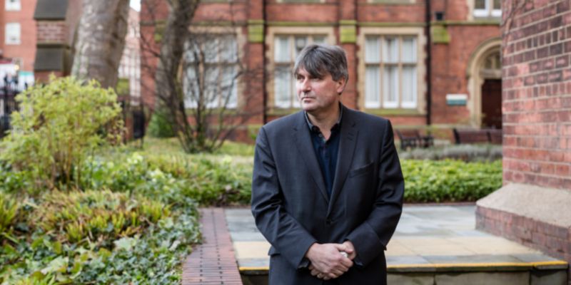 Simon Armitage stands wearing a black suit.