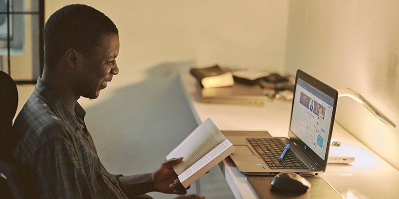 A online learner at home, using as laptop and referring to a book.