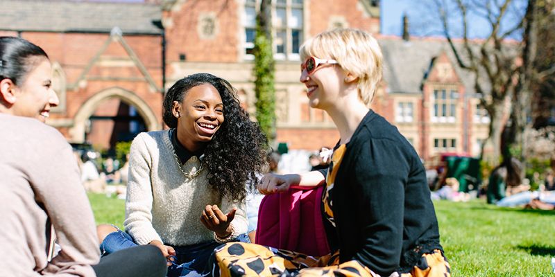 Three students sit in the park on campus