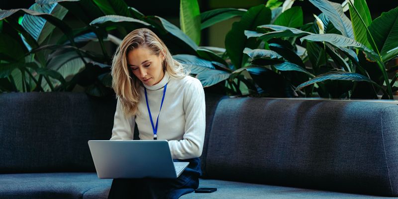 A person sat looking at a laptop with large lush plants in the bakgrounf.