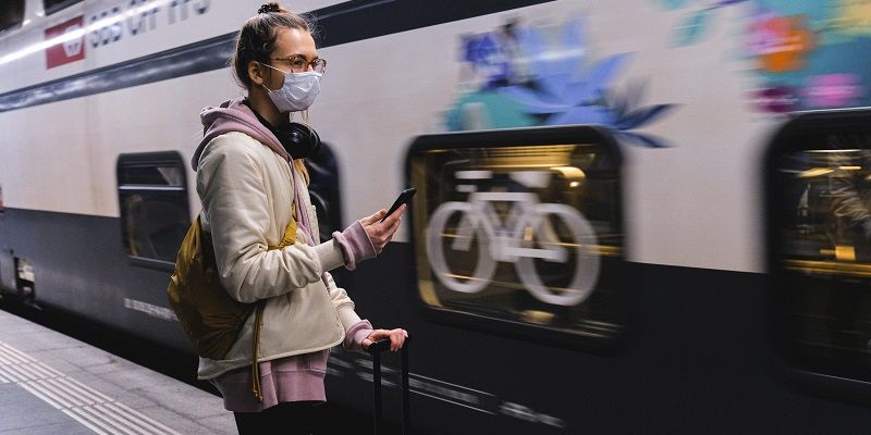 A person on a railway platform holding a mobile phone and luggage next to a moving train