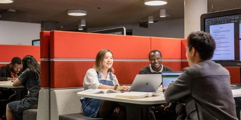 Three students doing group work together in a booth in the library.