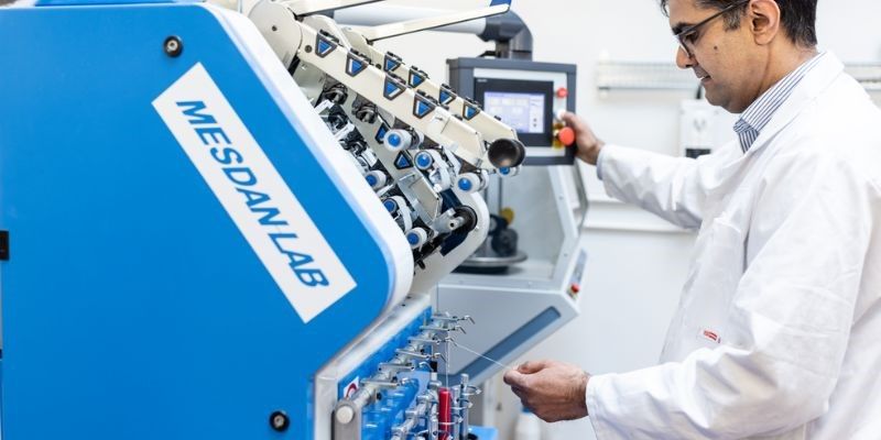 A lab techinian in a white lab coat operating the Yarn Spinning Line, a blue machine that produces white yarn.