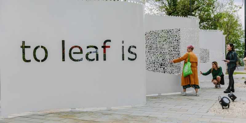 Students looking at the sculpture &#039;Curtain&#039; by Juanjo Novella, in the shape of a vertical wave and inscribed with the words 'to leaf is'