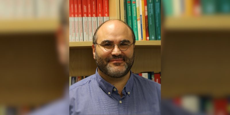 A head and shoulder photograph of Professor Alejandro Frangi in front of some bookshelves