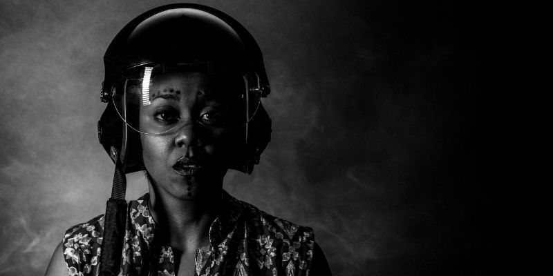 A dramatic black-and-white image of Keisha Thompson wearing an aviation helmet with dots drawn above their eyebrows