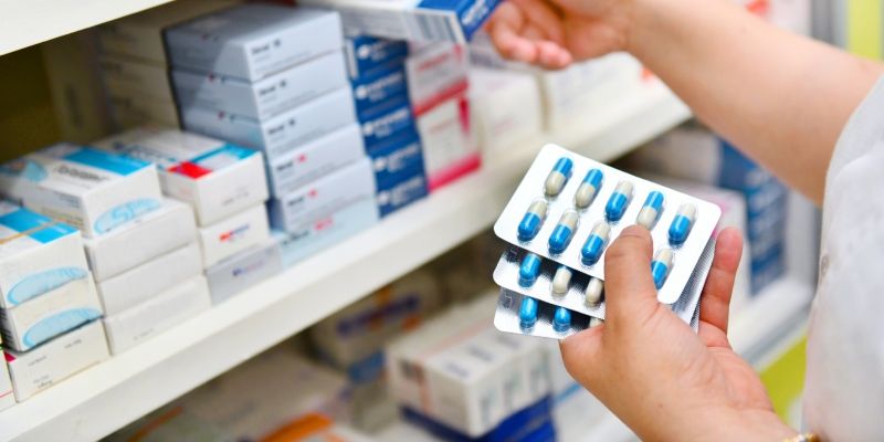 A pharmacist holding a medicine box and capsule pack in a pharmacy