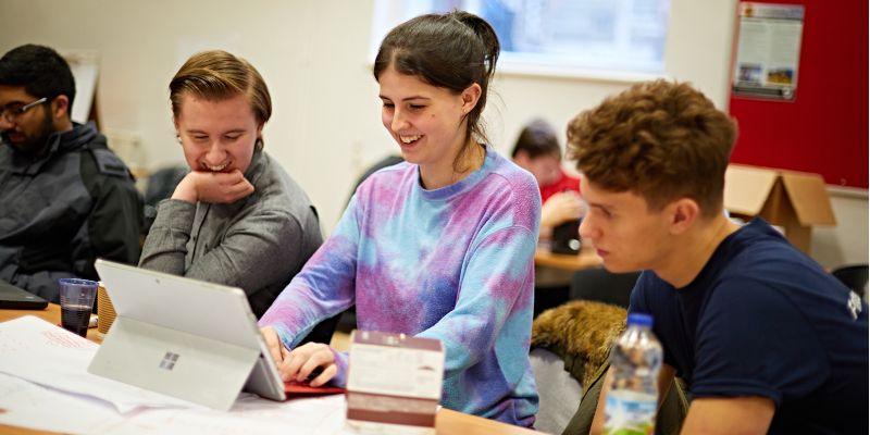 Three students on an apprenticeship programme in a classroom, studying a screen.