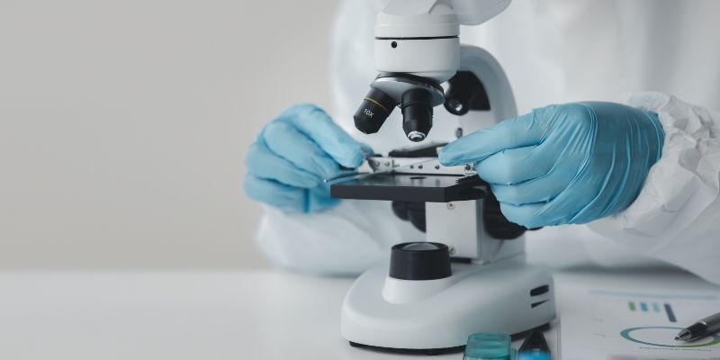 A researcher&#039;s gloved hands putting a slide into a microscope