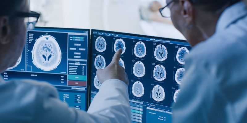 Two doctors looking at a computer screen showing brain scans