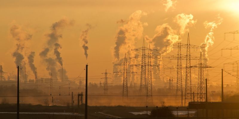 Electricity pylons and emissions from power plants against a yellow sky.