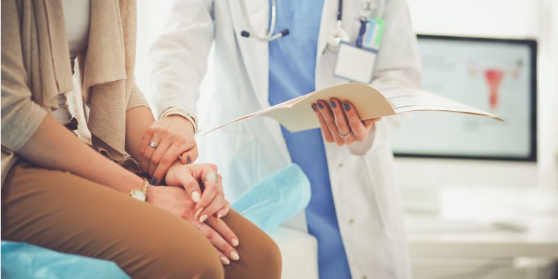 Patient sitting on the edge of a hospital bed and a doctor holding their arm and giving results.