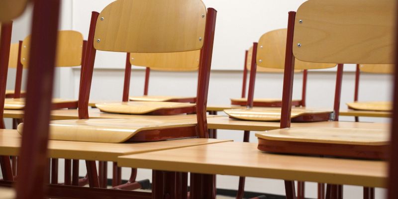 Empty classroom chairs placed on individual desks.