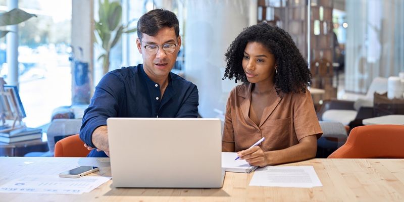Two people sat at a desk using a laptop