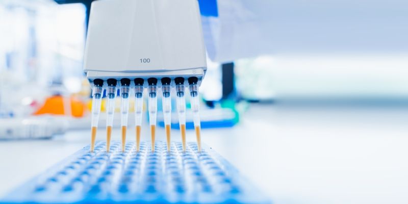 A machine with eight syringes containing coloured fluid which is being piped into testing trays