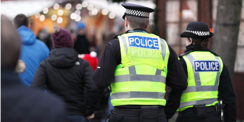 Two police officers, back to camera, walk down a crowded high street.