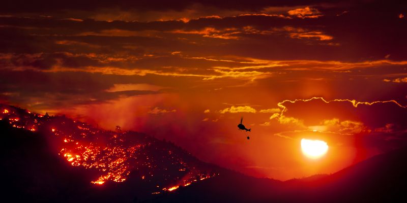 A helicopter flying over burning wildfires