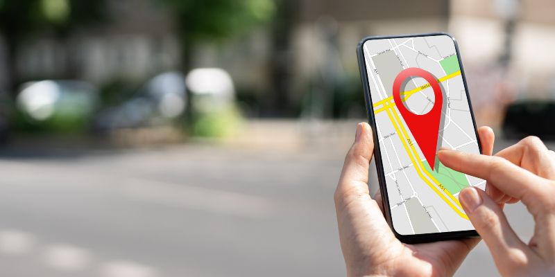 A person&#039;s hands holding a mobile phone with a location pin and map shown on the screen