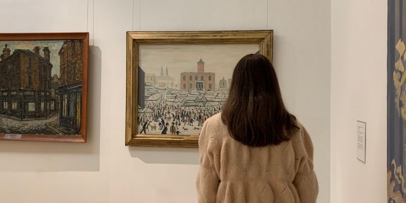 back of woman looking at a lowry painting