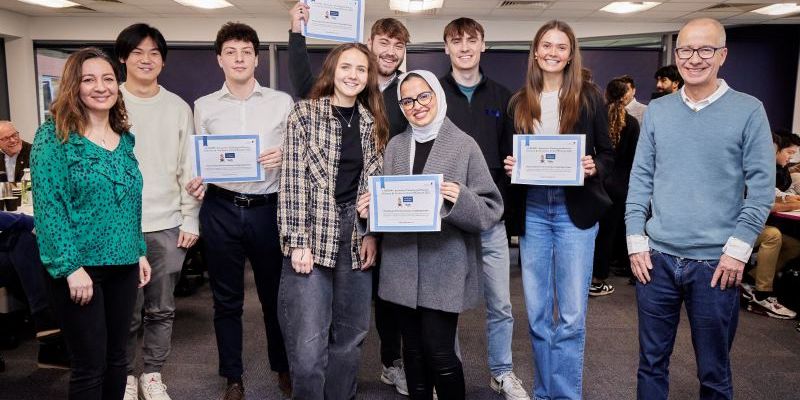 A group of students and two module teachers stood in front of the camera holding certificates