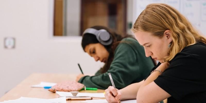Two students are sat at a desk, writing.