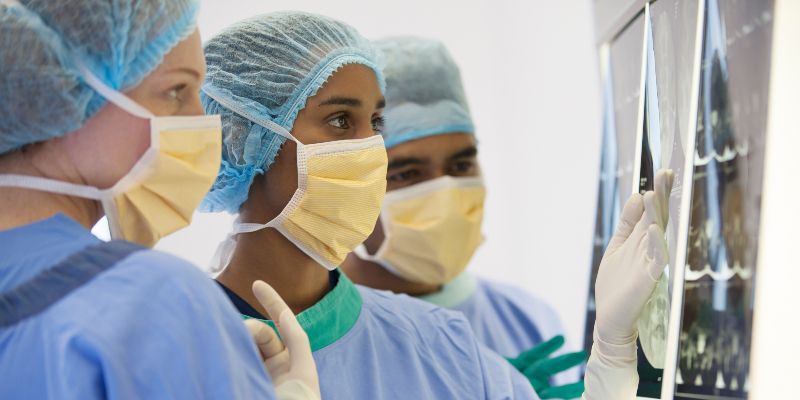 Doctors wearing surgical gowns and masks looking at medical scans