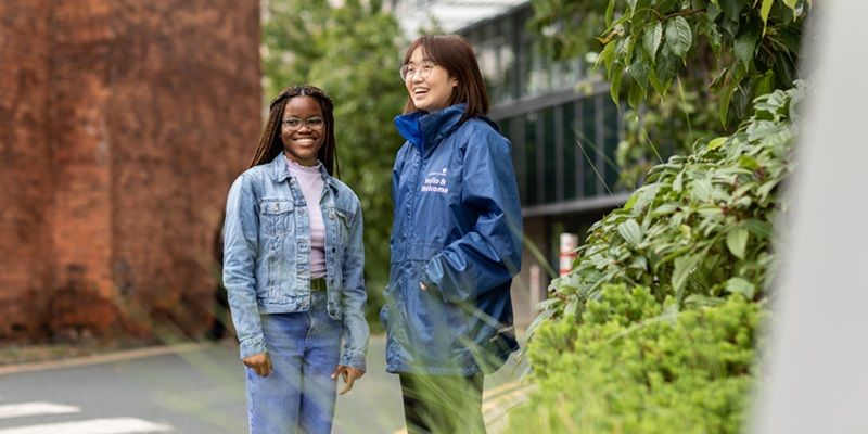 A student and Welcome ambassador looking around campus, stood in a green space between buildings