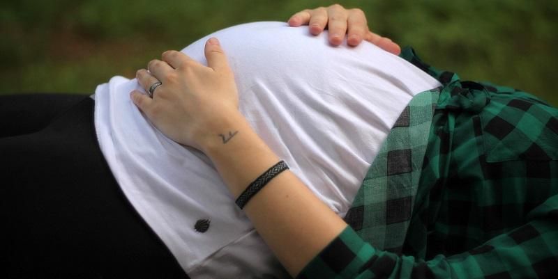 The images shows a pregnant woman lying down feeling her bump.