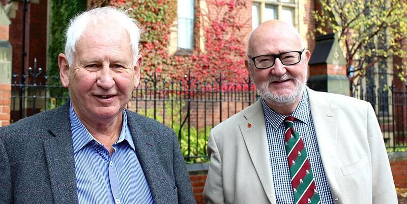 Two members of the Leeds Alumni community stand in shirts and jackets outside the Great Hall at a reunion.