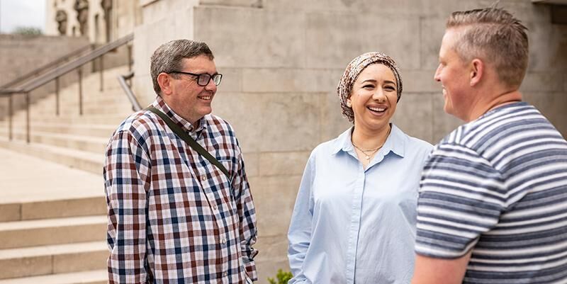 Three people standing together laughing with the Parkinson Building steps in the background.