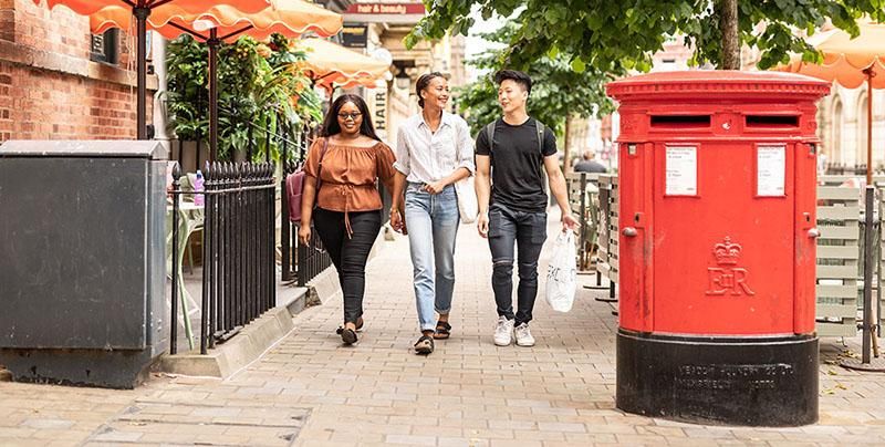 Three students walking next to a red post box in Leeds city centre