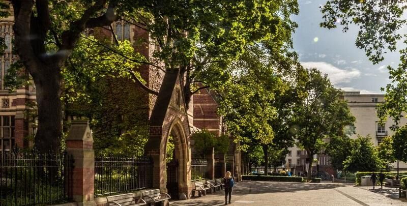 A person walks down the path outside the Great Hall on a sunny day.