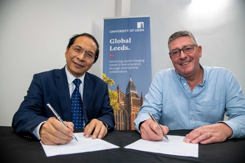 Two people are signing the paper agreement at a desk with a University of Leeds banner behind them.