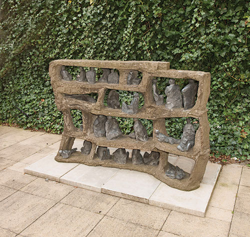 The artwork Limbo stands in front of an ivy covered wall. Lead pieces stand in an irregular tiered structure.