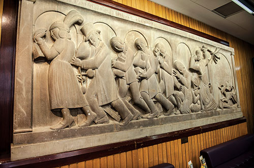 A stone frieze showing Christ expelling a group of moneychangers from the temple - some wearing contemporary attire.