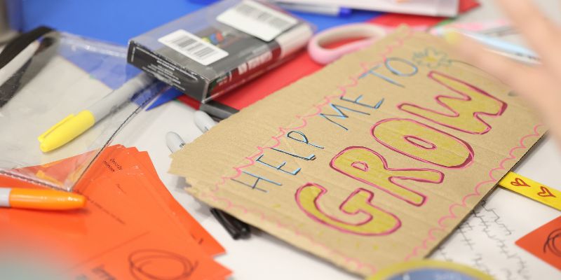 A piece of cardboard with 'Help me to grow' written on it.