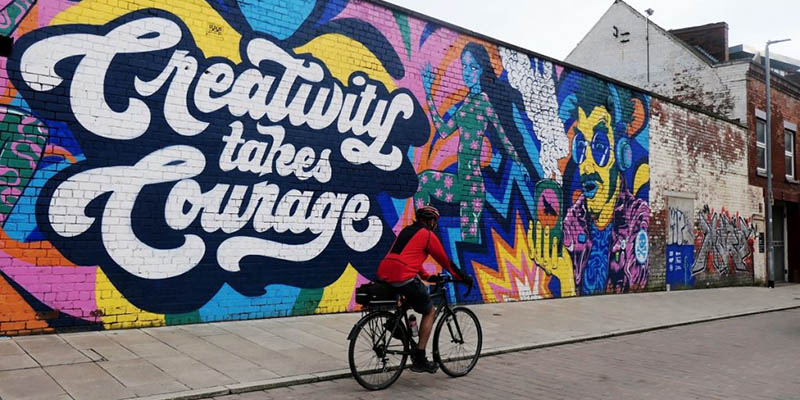 A painted wall which says Creativity takes courage. A person is cycling by.