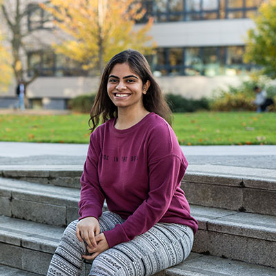 Student Hetasha Gopalani smiles while sitting on steps on campus.