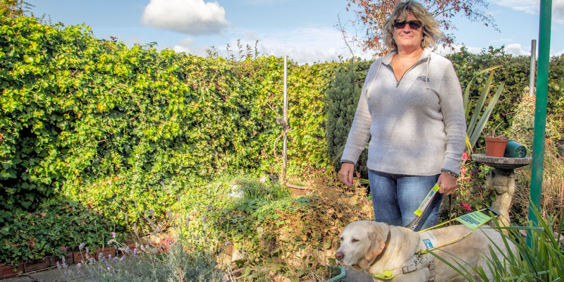 Helen Walker and her guide dog Tasmin stand smiling in a garden