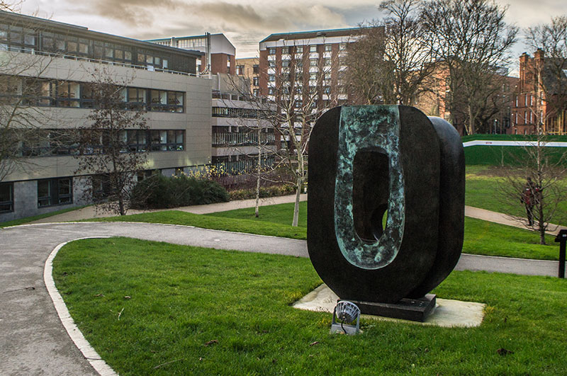 Dual Form by Barbara Hepworth stands in the middle of grass. Made of bronze, it is a rounded rectangle with a hole in the middle and pierced hollows.