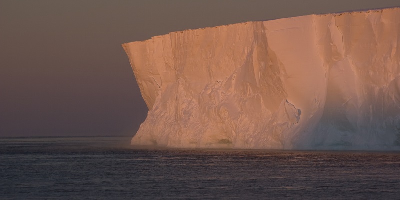 Ice shelf extending over the oceans. The ice shelf is a pink colour due to the setting sun.