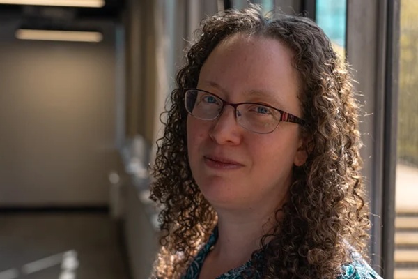 Headshot of Jenny Sexton, wearing glasses and looking at the camera in a corridor.