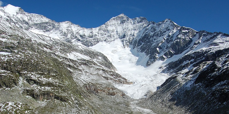 Odenwinkelkees glacier   with bare rocky mountainside on either side with bright blue sky in the background. 