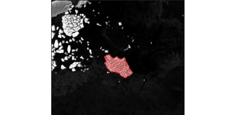 Aerial image of an iceberg highlighted in pink. The surrounding ocean is black and white floating icebergs surround the highlighted iceberg.