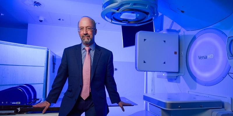 The image shows Professor David Sebag-Montefiore standing by the side of a large radiotherapy machine
