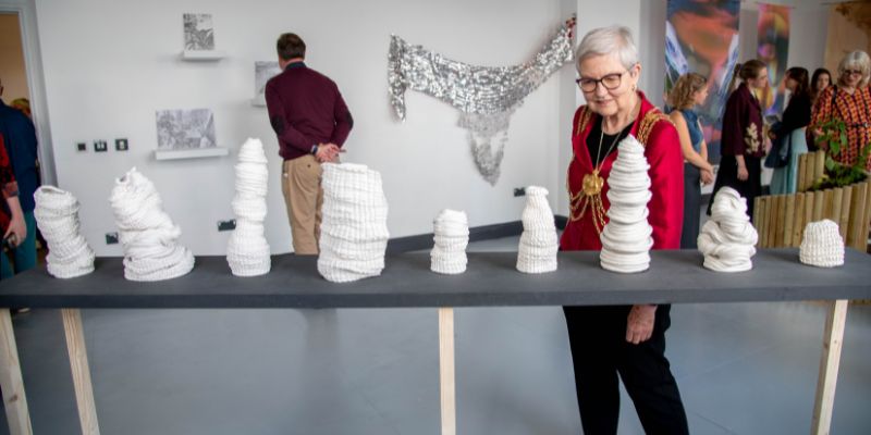 Lord Mayor of Leeds Al Garthwaite, wearing her gold chains of office, inspects a row of small white sculptures