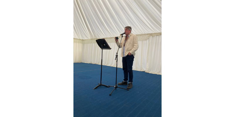 Man inside a marquee stood at a microphone reading from his phone